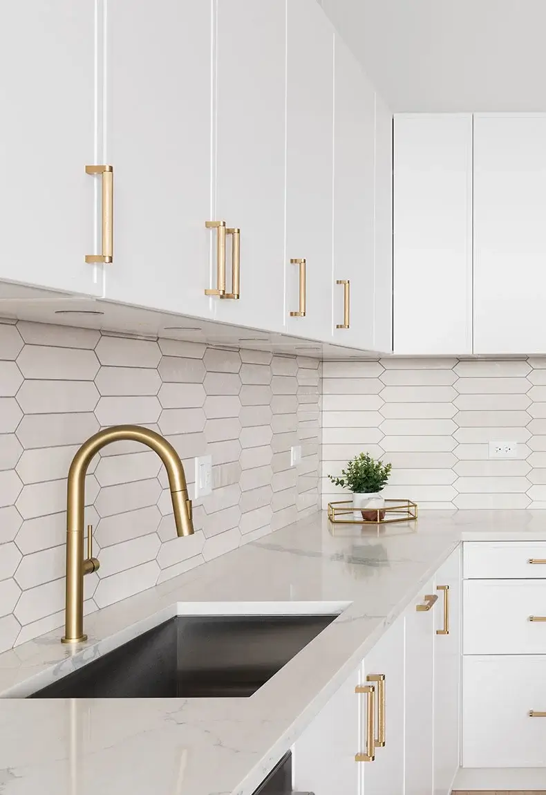 White kitchen with gold accents, including a gold faucet, handles, and a picket-style backsplash.