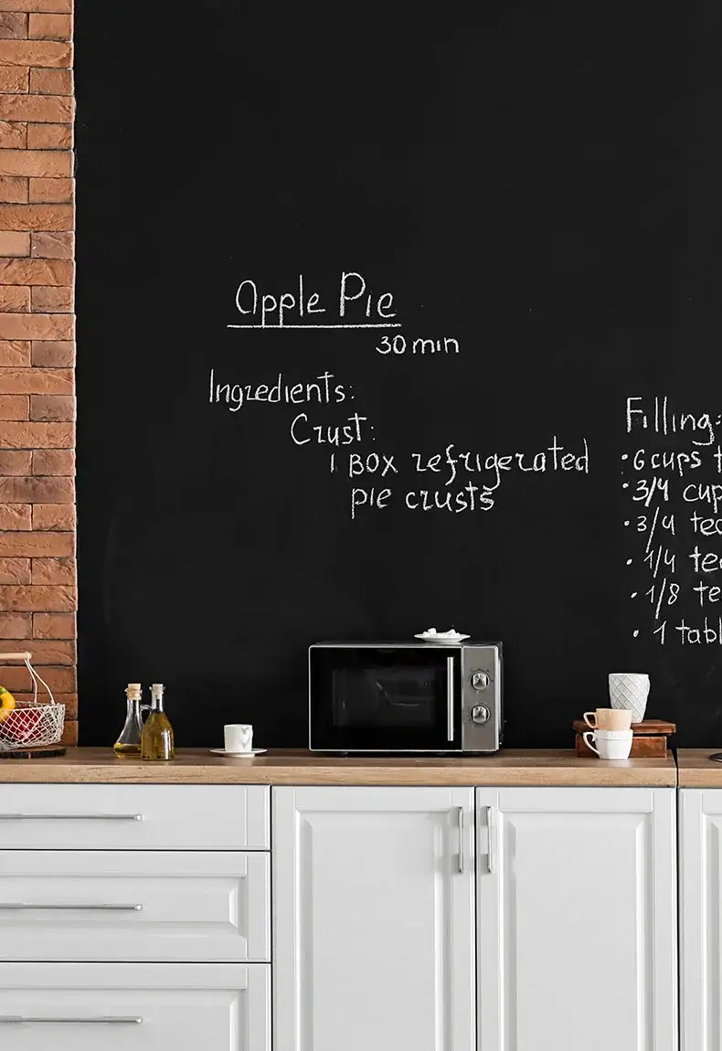 Kitchen with chalkboard wall backsplash, brick walls, white cabinets, and kitchen appliances.