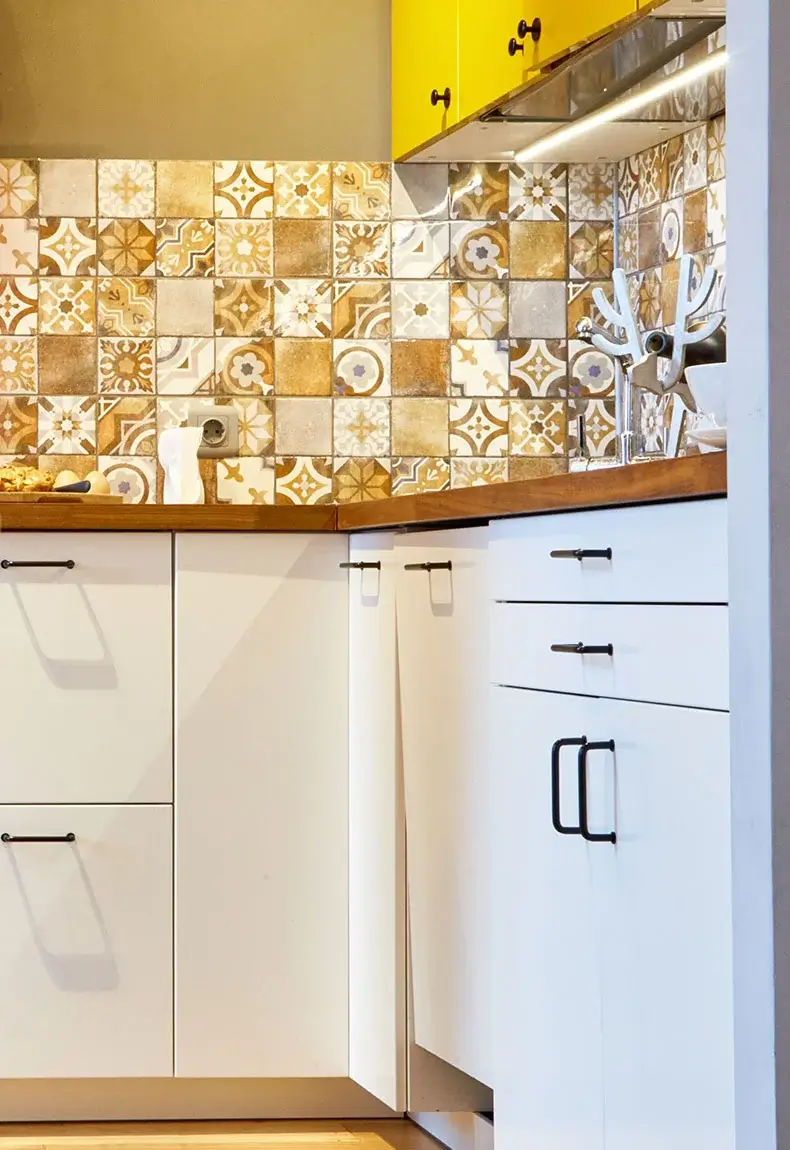 New age kitchen with bright yellow, brown, and white mosaic backsplash patterns, brown countertops, and white cabinets.