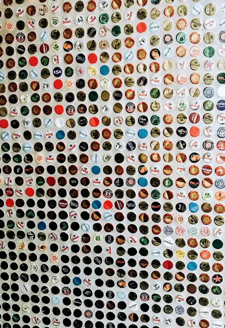 Multi-colored bottle caps attached to wall for kitchen backsplash decor.