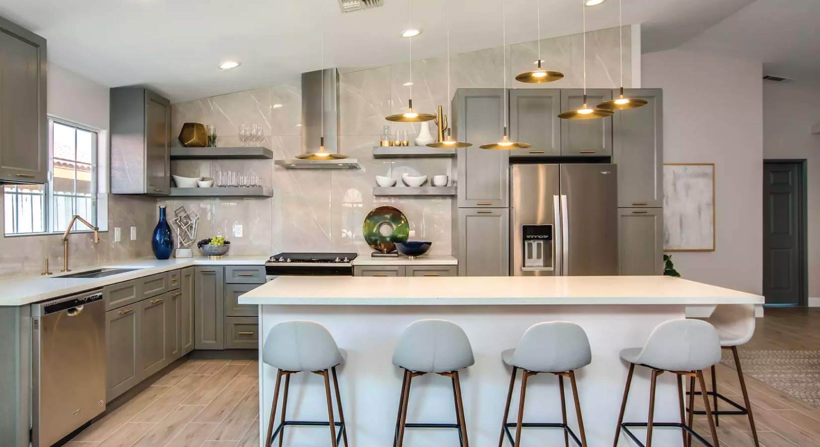 Gray shaker kitchen cabinets in modern kitchen with brass pendant lighting and marble backsplash.