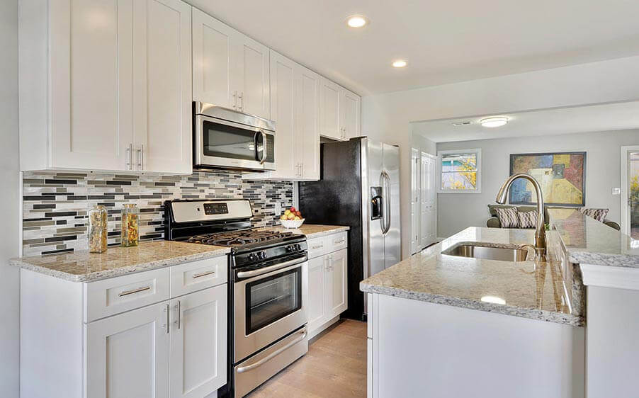 Modern galley kitchen with white cabinets, granite countertops, and white and gray tiled backsplash.