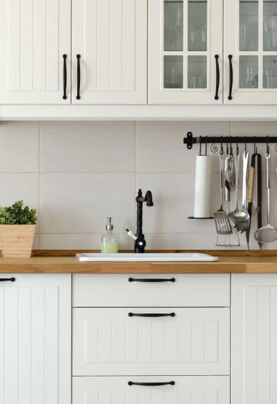 Black bard-inspired pulls on white beadboard kitchen cabinets.