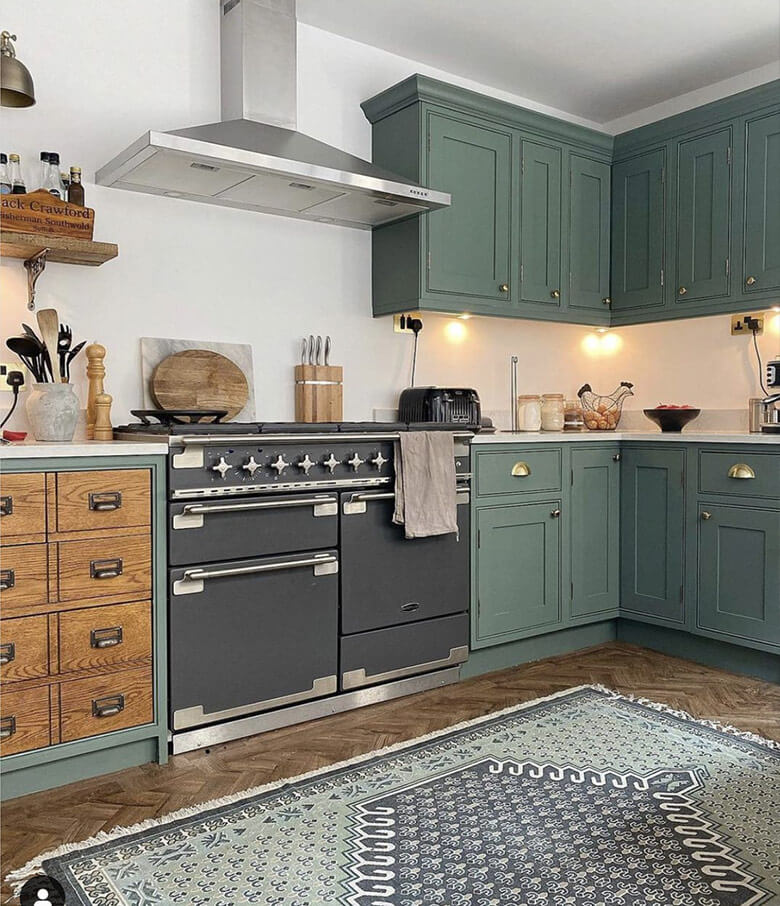 Bohemian vintage kitchen with dark green cabinets and oversized black oven range.