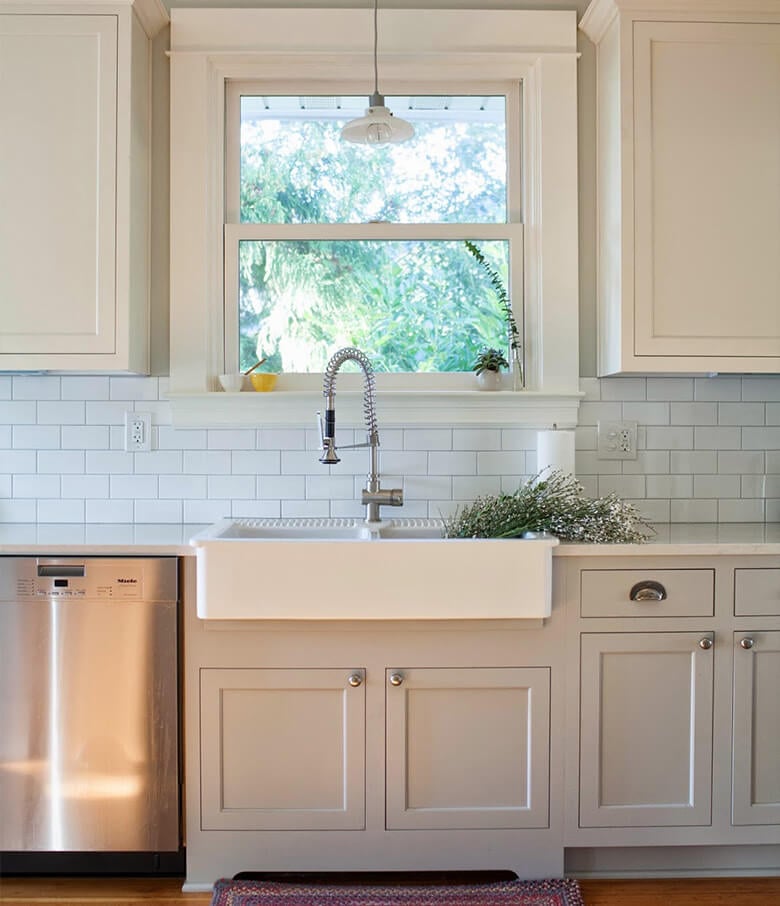 Farmhouse kitchen with white upper and gray lower cabinets and traditional white farmhouse sink.