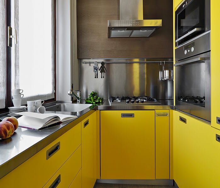 Small kitchen with illuminating yellow slab cabinets and stainless steel backsplash.