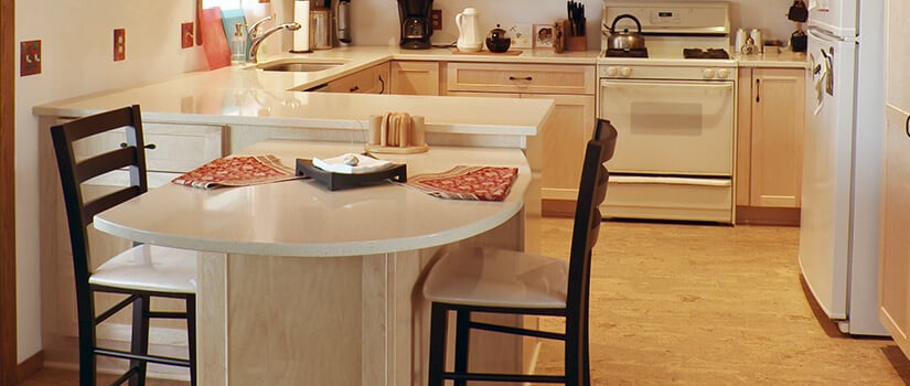 Cork kitchen flooring with wood cabinets and white countertops.