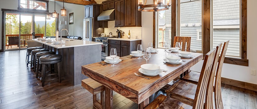 Farmhouse style kitchen with exposed wooden beams, wooden table, and dark cabinets.