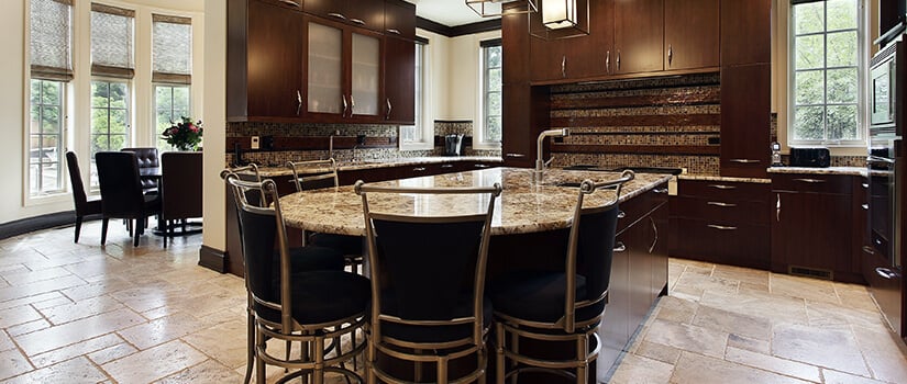 Modern kitchen with travertine flooring, dark cabinets, and granite countertops.