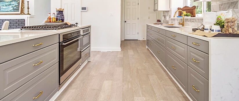 Modern kitchen with wood-look vinyl flooring, gray cabinets, and stainless steel appliances.