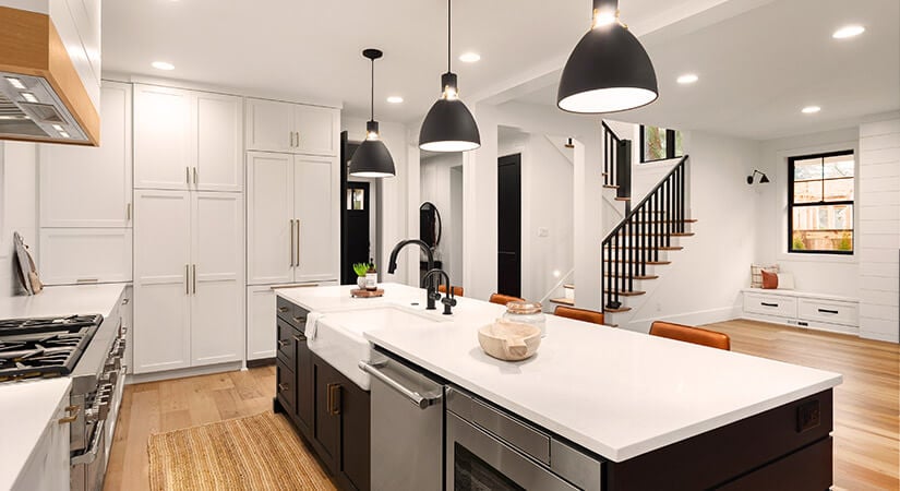 Three pendant lights with black shades over kitchen island with black cabinets.