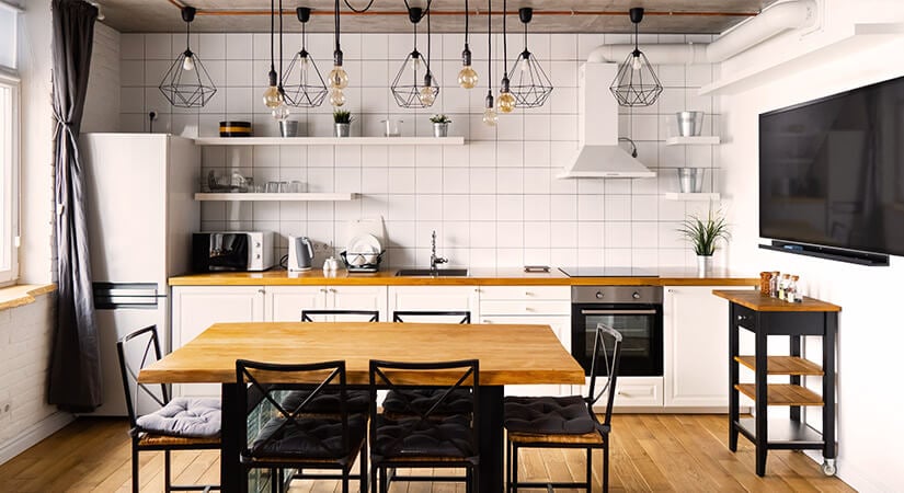 Multiple bare-bulb and cage pendant lights over white galley kitchen and wood dining table.