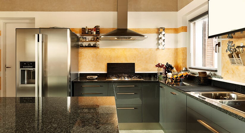 Kitchen with shiny black countertops, stainless steel appliances, and lacquered teal cabinets with gold hardware.