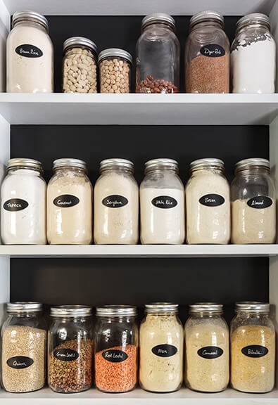 Labeled glass containers in organized kitchen cabinet.