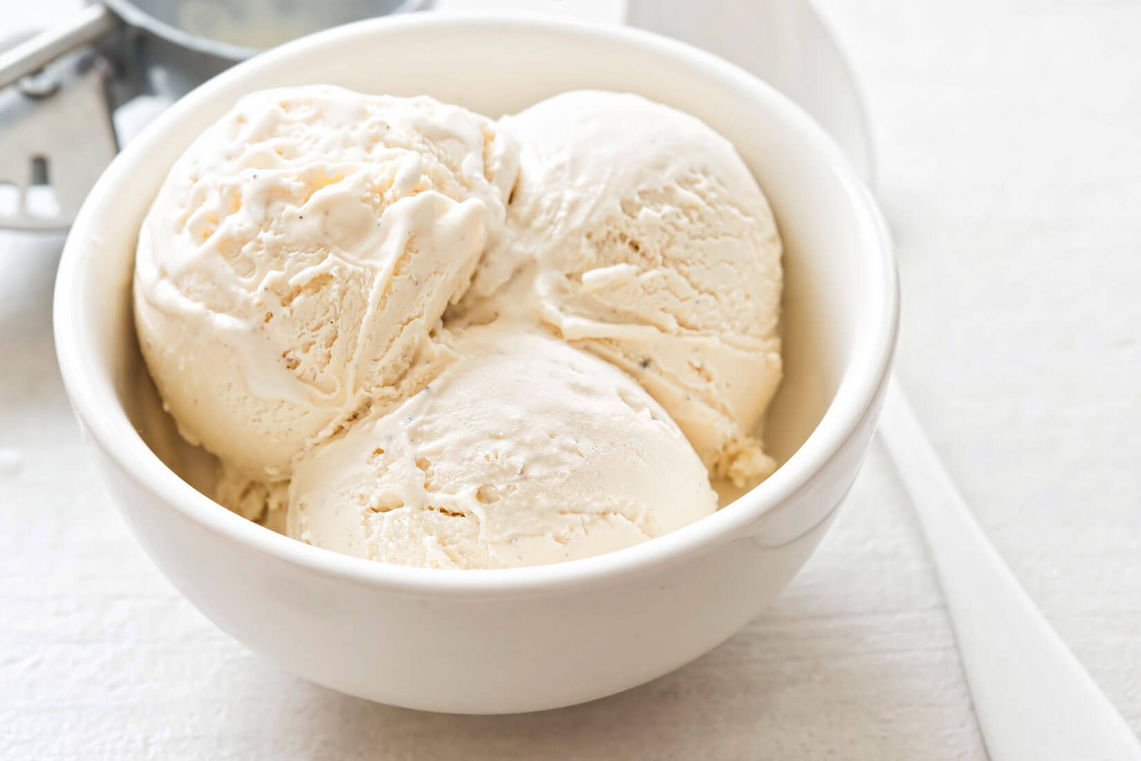 White bowl with three scoops of vanilla ice cream.