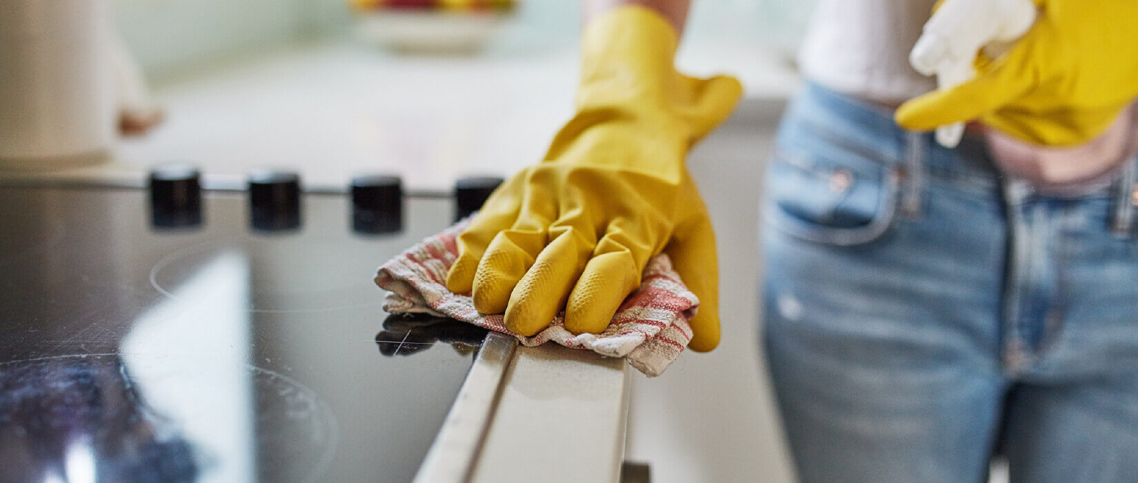 Women with yellow rubber gloves wiping stove top