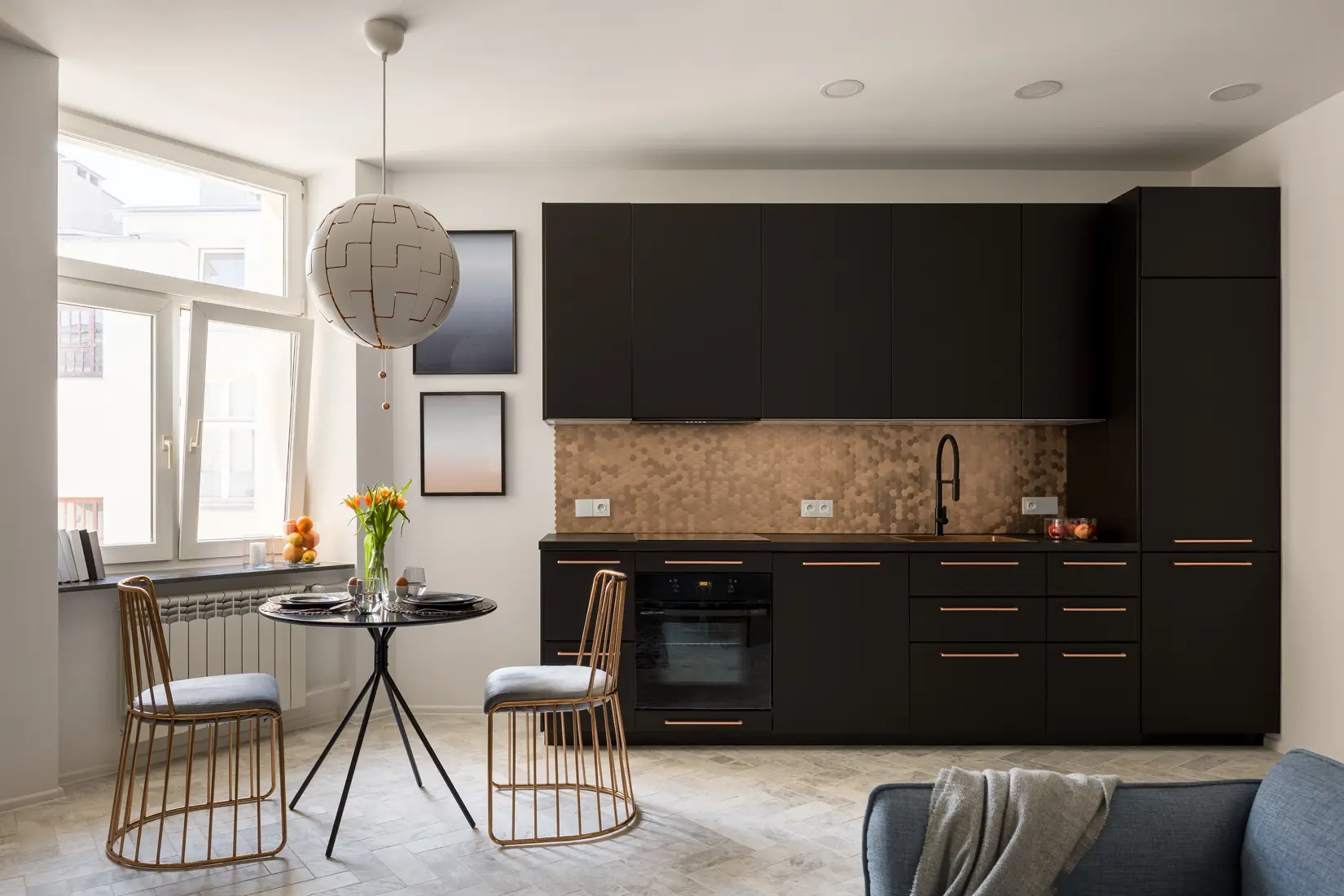 A black kitchen with copper tile backsplash and flowers as kitchen decor.