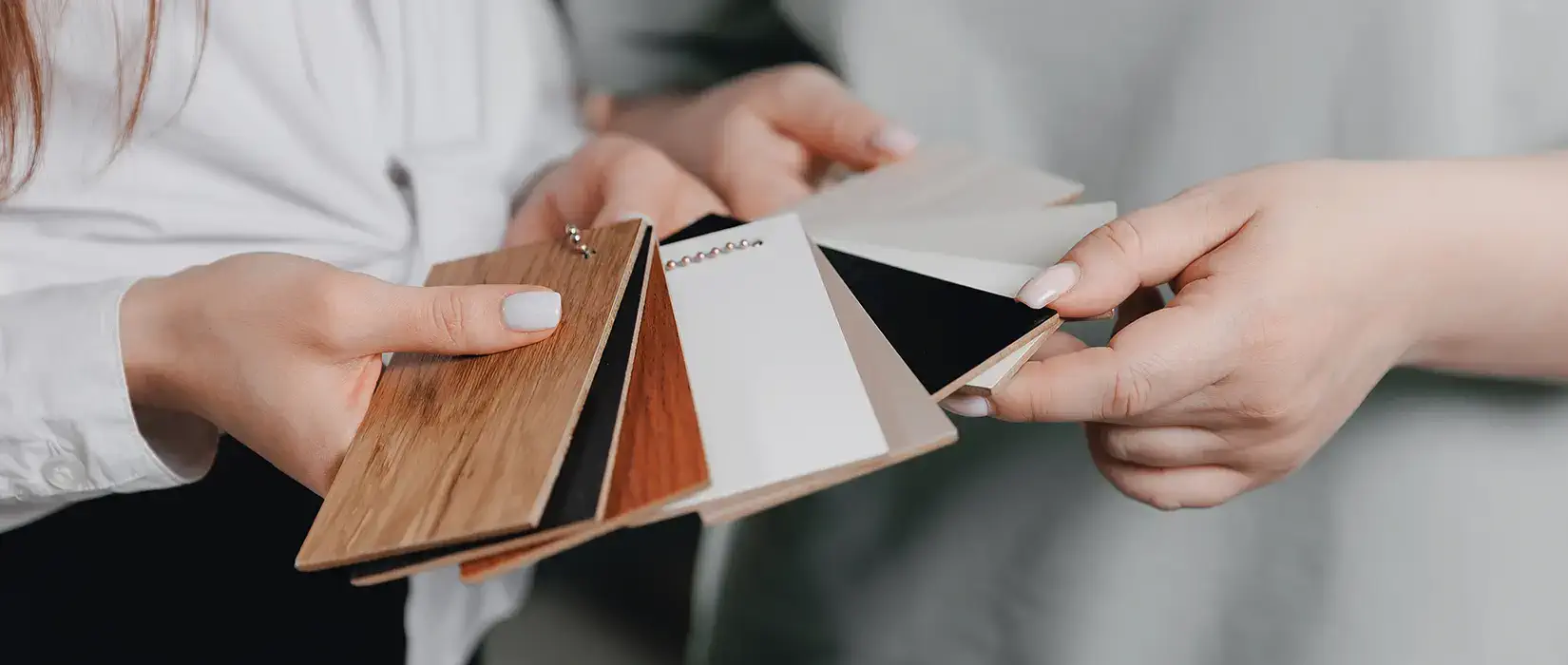 Two women comparing laminate vs. wood cabinet swatches.