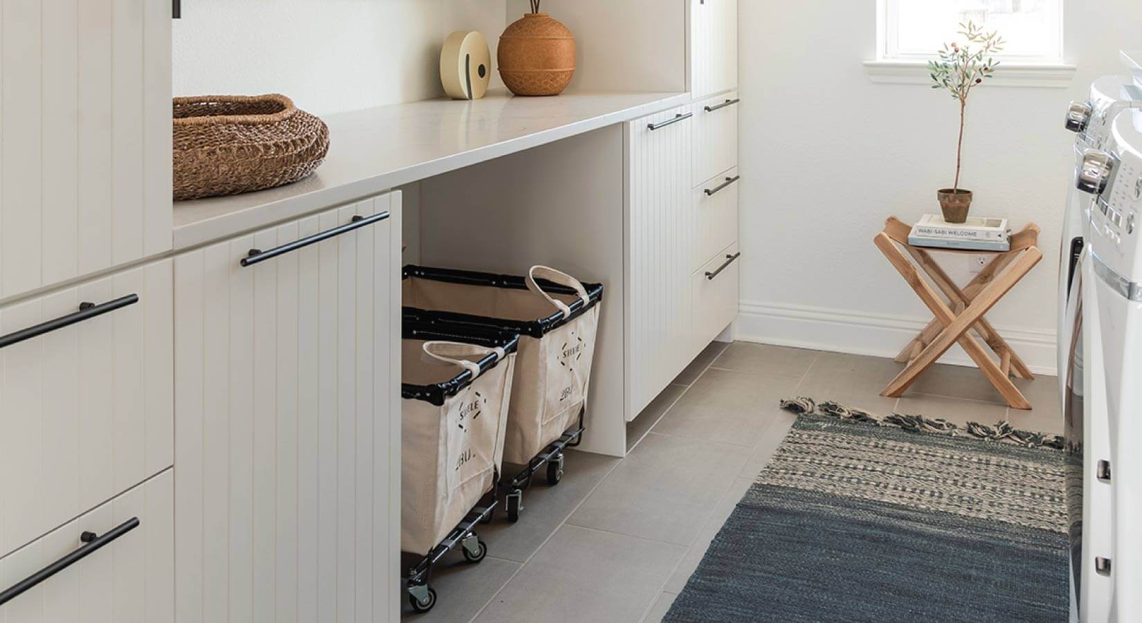 Laundry room with white beadboard cabinets, rolling laundry bins, and blue rug.