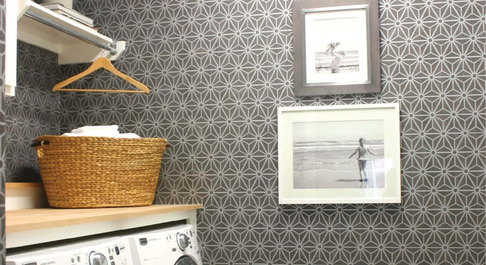 Laundry room with folding table on top of appliances, gray patterned wallpaper, and family photos.