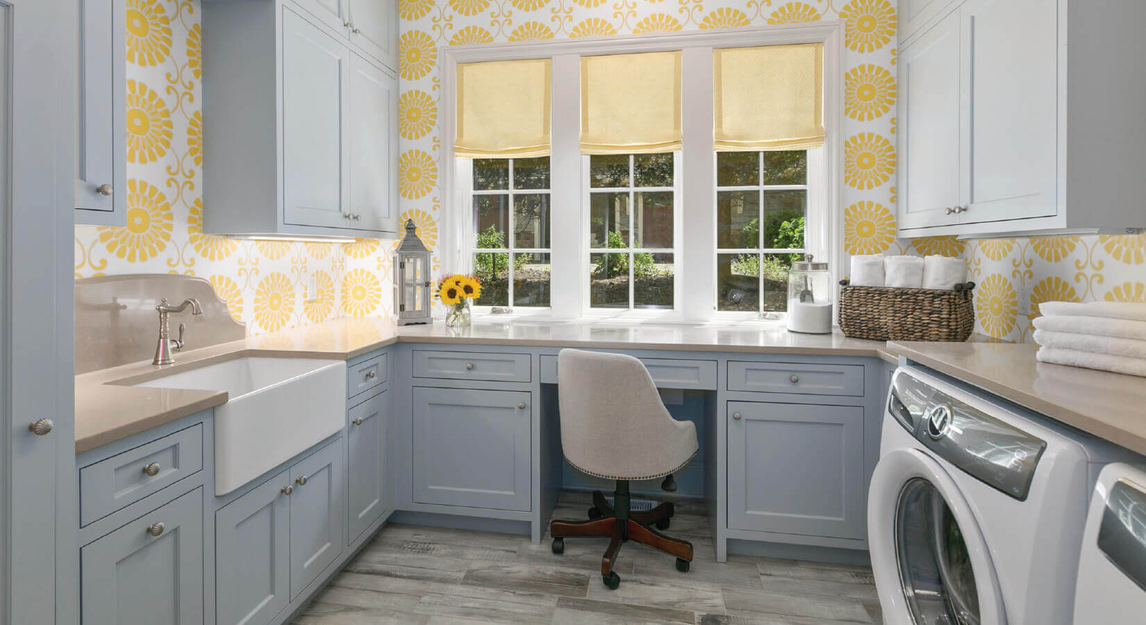 Laundry room with pastel blue cabinets, farmhouse sink, and yellow flower wallpaper.