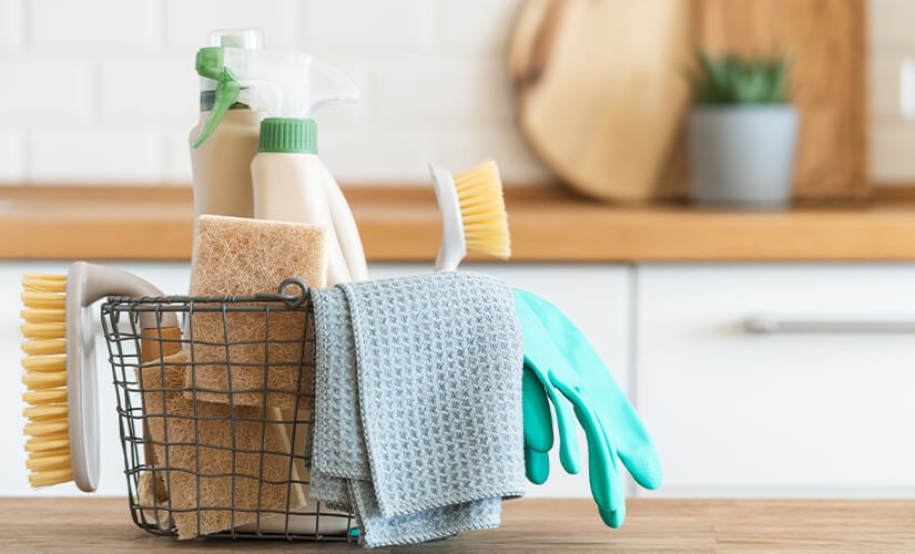Small black wire basket with gloves, sponge, brush, and cleaning products.