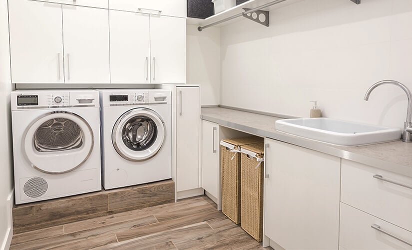 Laundry room with white cabinets and wicker hampers under gray countertop.