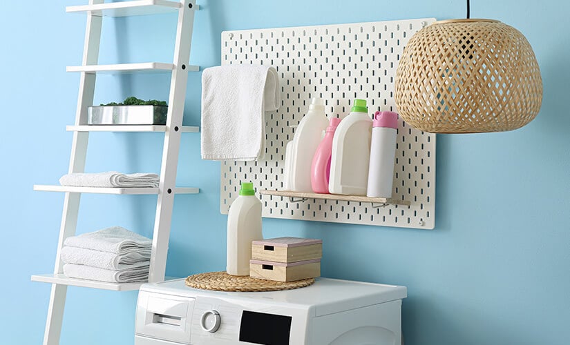 Shelf ladder and white pegboard above washing machine with laundry detergents and hand towel.