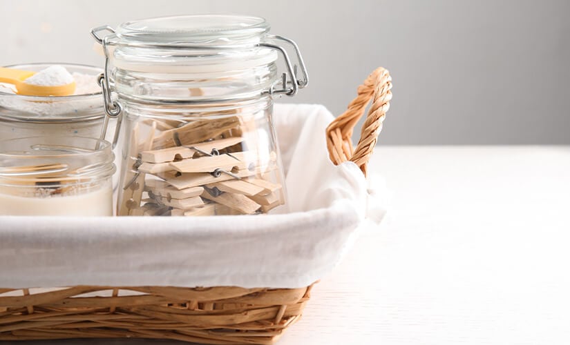 Wicker basket with glass jars filled with clothes pins and laundry detergent.