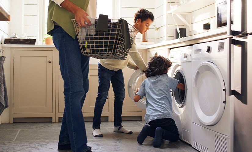 Two young boys helping father load washing machine.