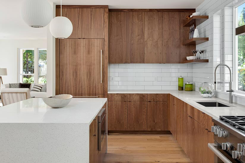 Modern kitchen with walnut natural wood cabinets, white countertops and subway tiles, and white orb pendant lights over kitchen island.