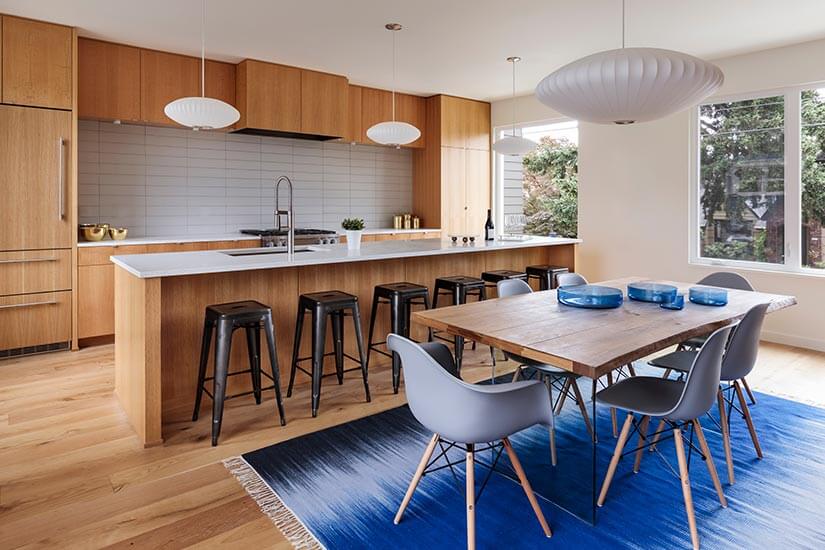 Mid Century Modern kitchen with light oak wood cabinets and flooring, white countertops, and lantern-style pendant lights.