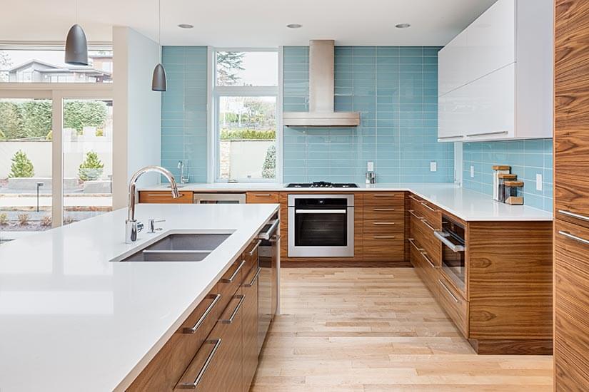 Modern kitchen with walnut cabinets, white granite countertops and a light blue subway tile backsplash.