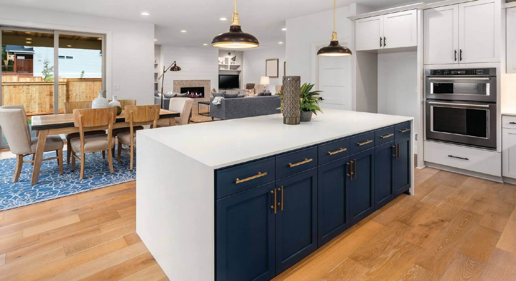 Kitchen island with white waterfall countertop and navy blue cabinets with gold hardware on light wood floor.