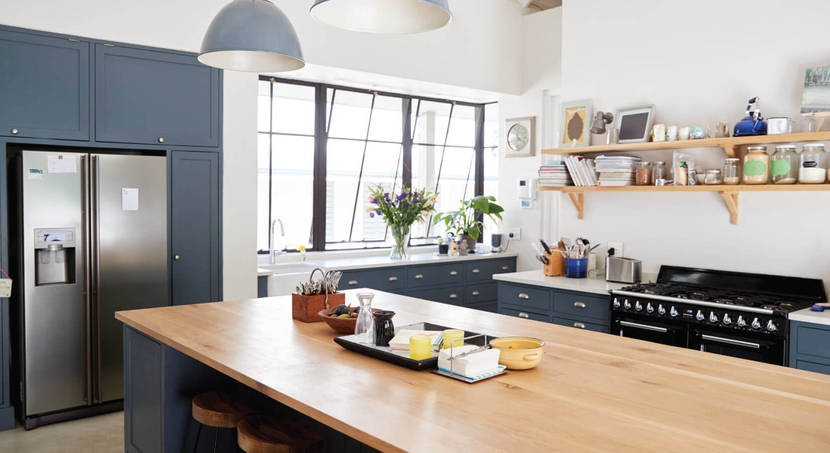 Kitchen with dark gray-blue cabinets, large butcher block island, and open wood shelves.