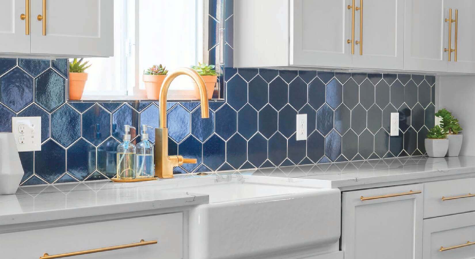 Navy blue hexagon-shaped tile backsplash with copper faucet and white cabinets with copper hardware.