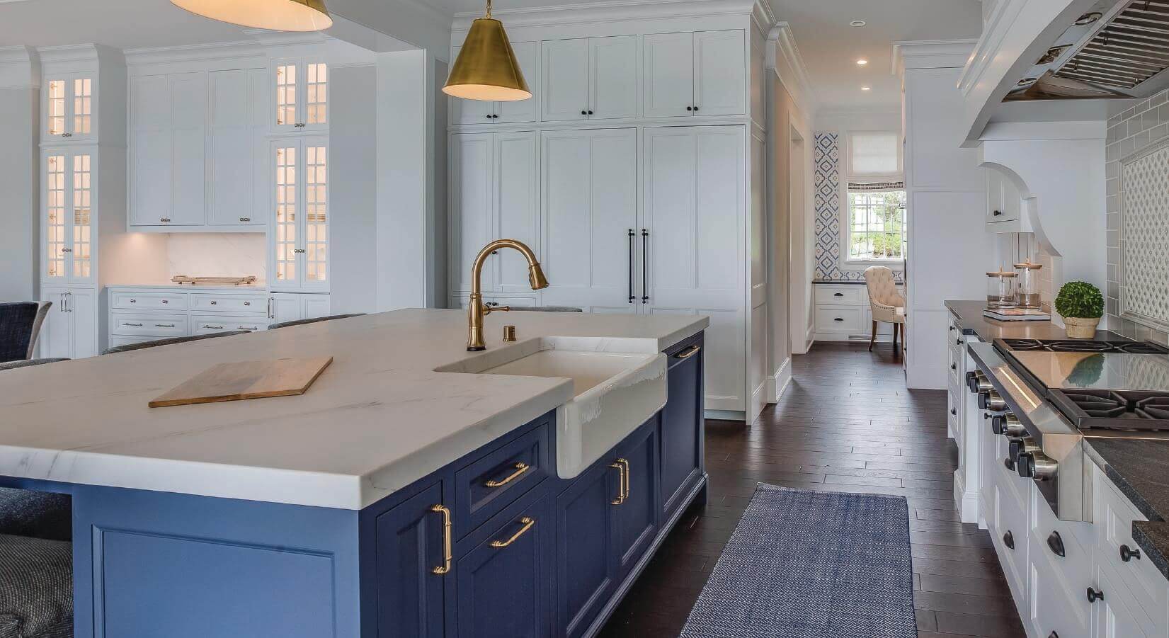 Kitchen with large marble kitchen island with farmhouse sink, dark blue cabinets, and copper faucet and cabinet hardware.
