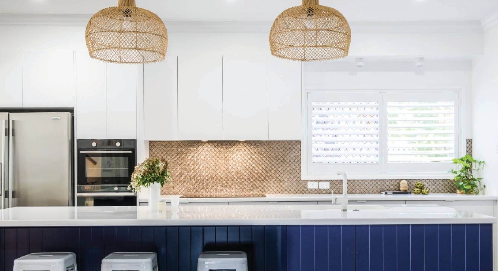 Kitchen with navy blue island with rattan light fixtures and copper backsplash.