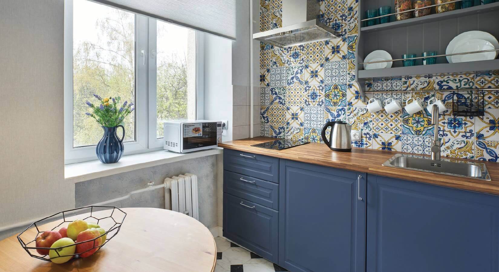Small kitchen with navy blue cabinets, butcher block countertops, and yellow and blue Moroccan patterned backsplash.