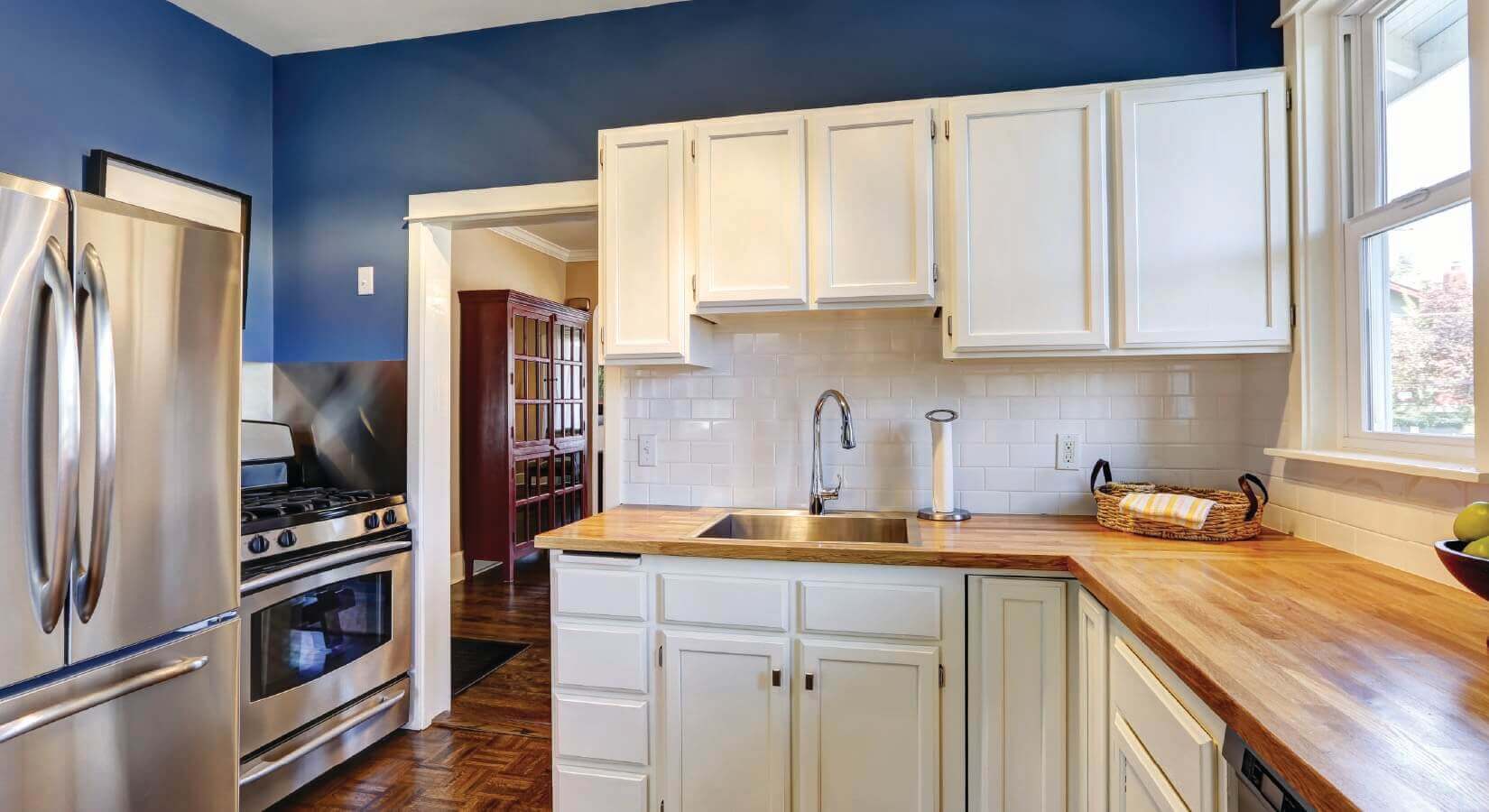 Kitchen with white cabinets and backsplash, butcher block countertops, and navy blue walls.