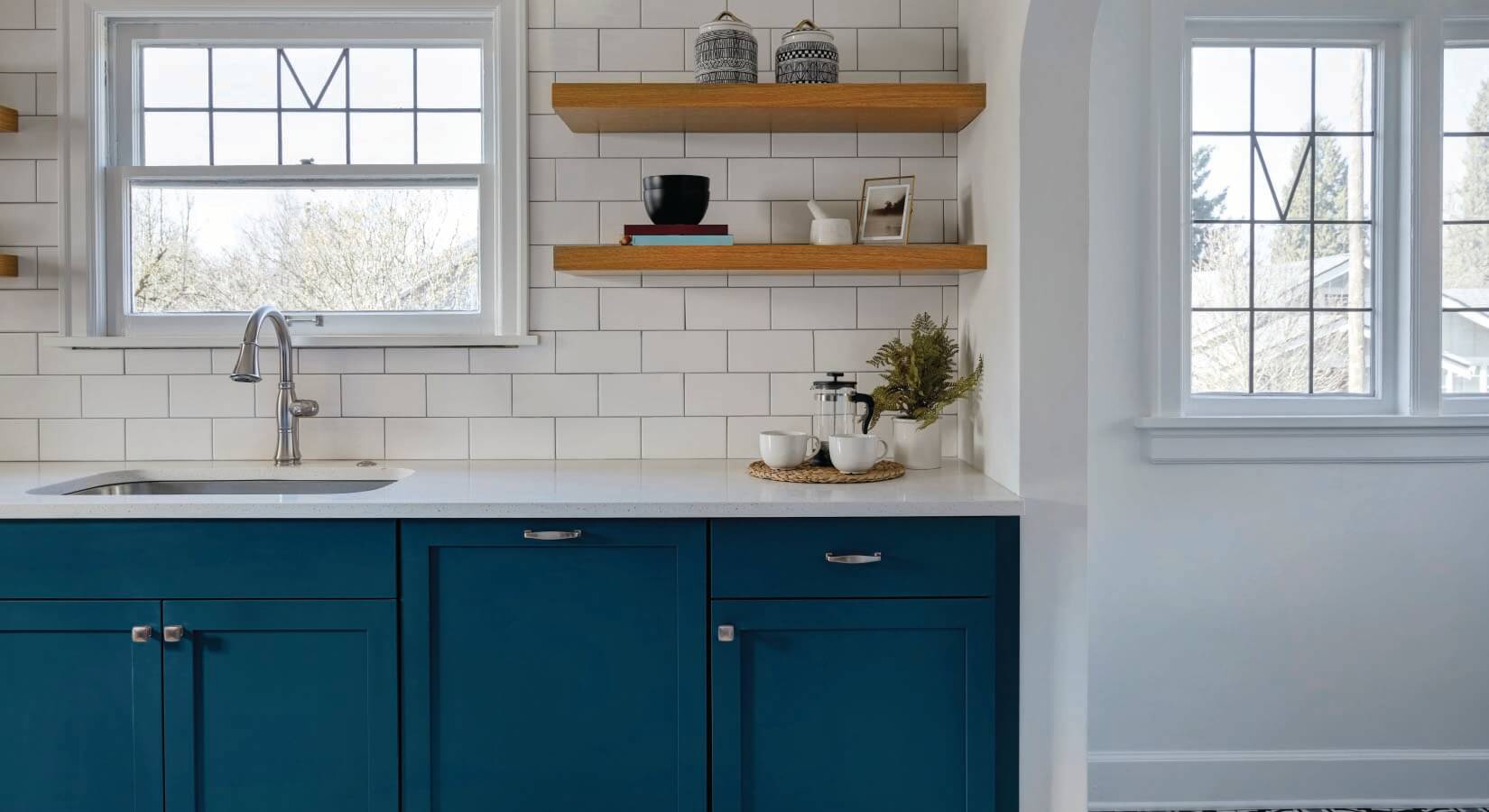 Kitchen with navy blue cabinets, white countertops, wood open shelving, and white subway tile backsplash.