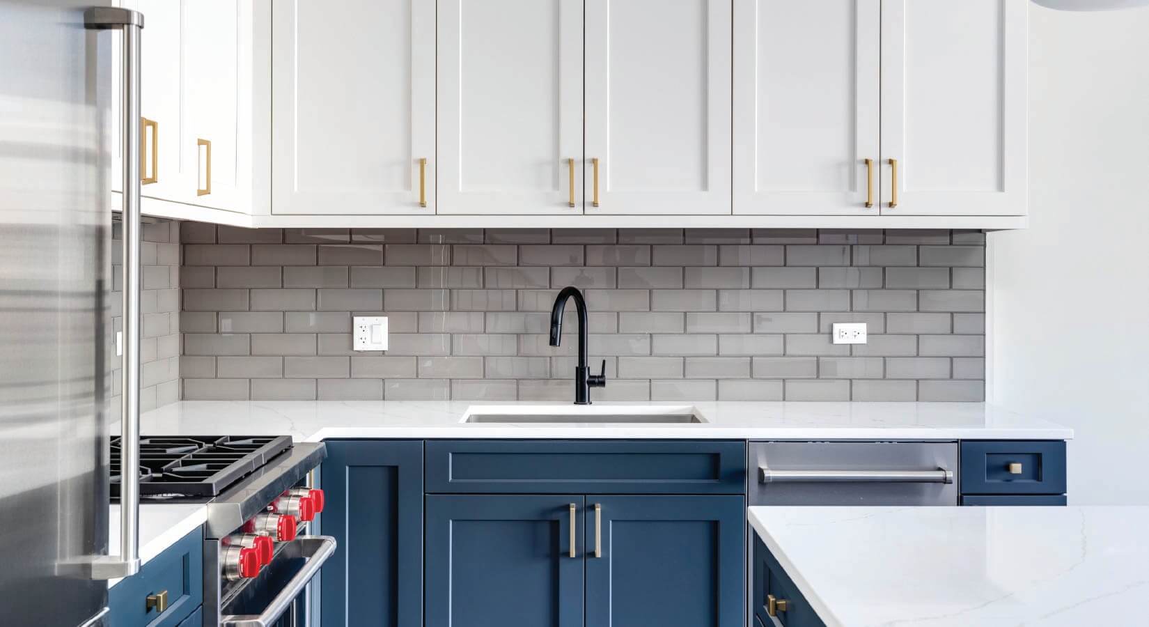Kitchen with dark blue lower cabinets and white wall cabinets with gold hardware.