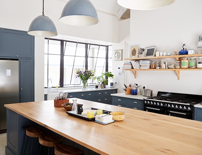 Dark blue modern kitchen with butcher block countertop and wooden open shelves.