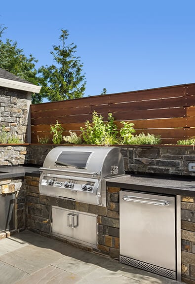 Outdoor kitchen with stone walls, built in grill, and herb garden.