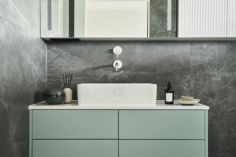 Mint green floating vanity with white sink installed on wall with gray stone tile.