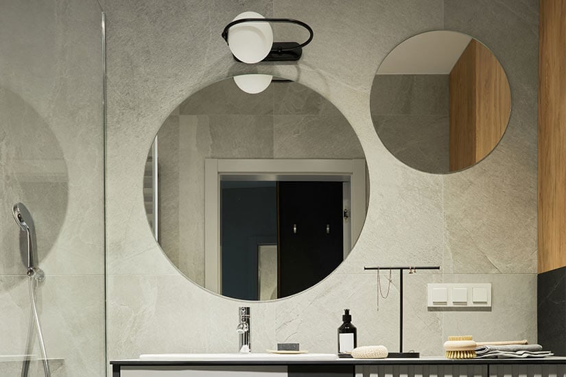 Bathroom vanity with one large circle mirror and one smaller circle mirror to the right.