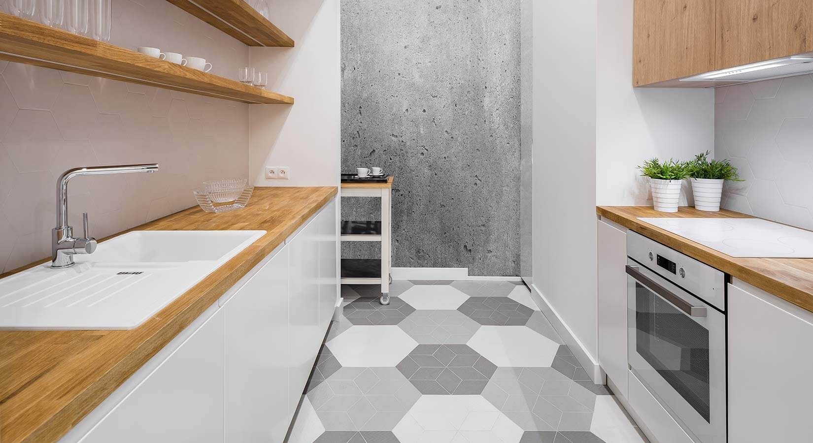 Small galley kitchen with white cabinets, wood countertop, and gray and white patterned floor tile.