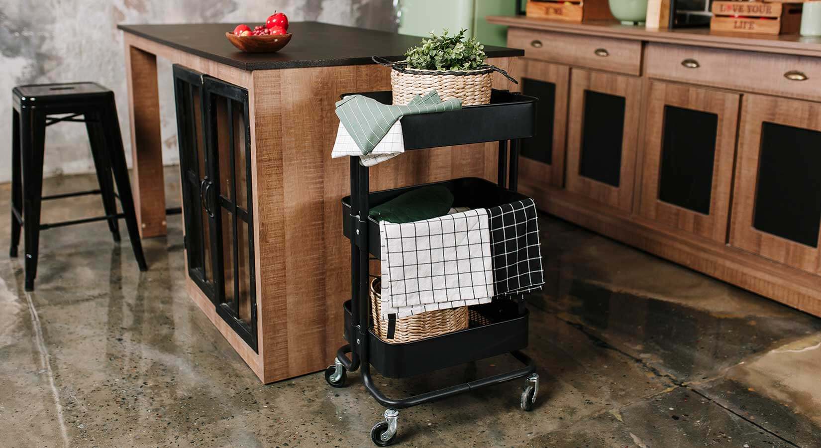 Black kitchen cart with plants and kitchen towels beside small kitchen island.