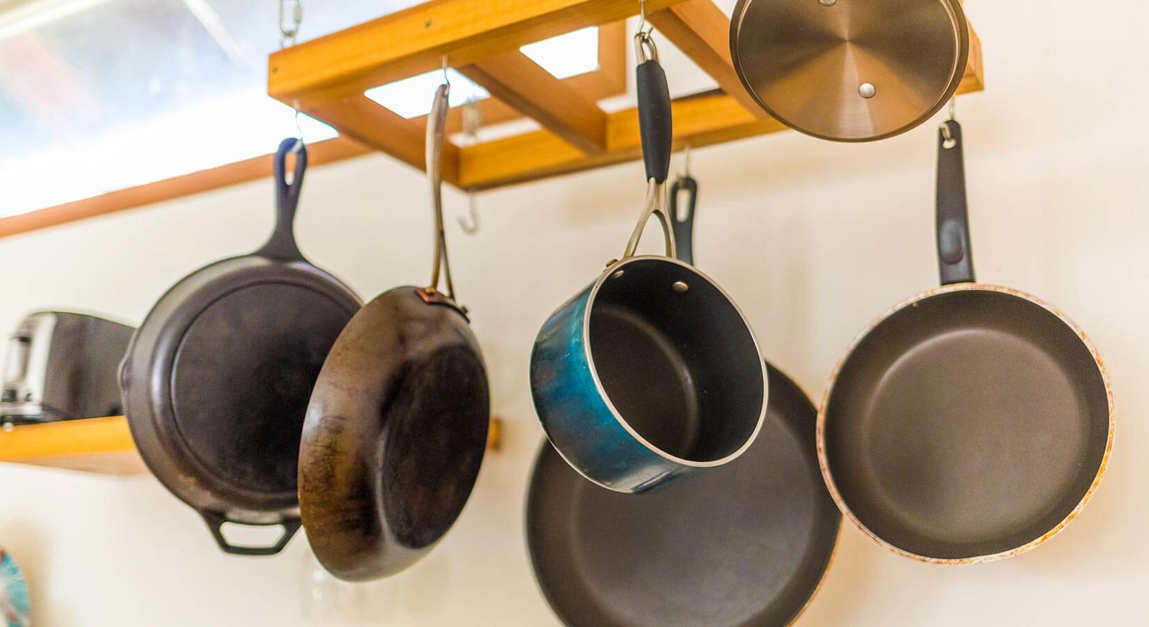 Six pots and pans hanging from wood ceiling rack.