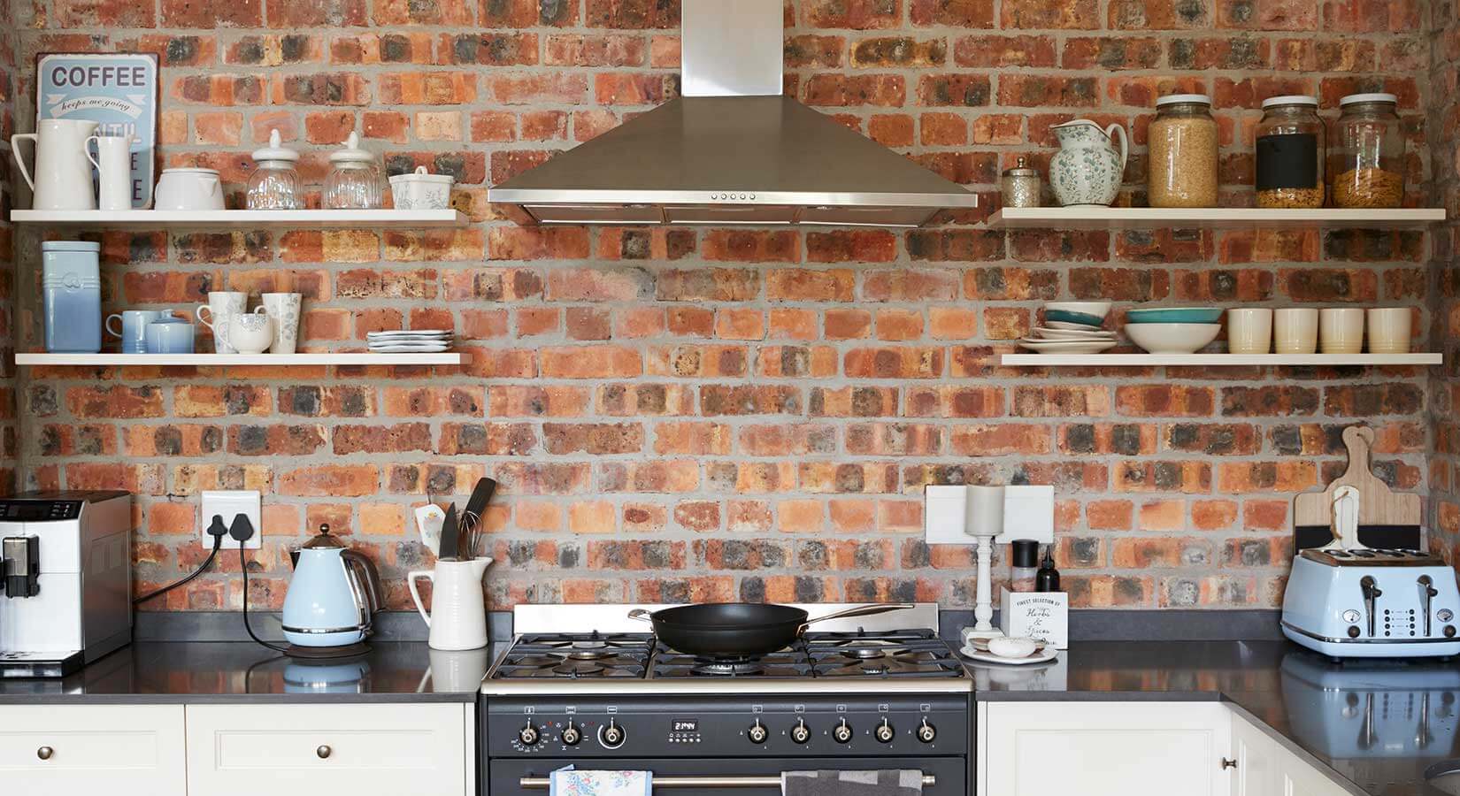 Brick kitchen wall with stove top and range in center and two open shelves on each side.